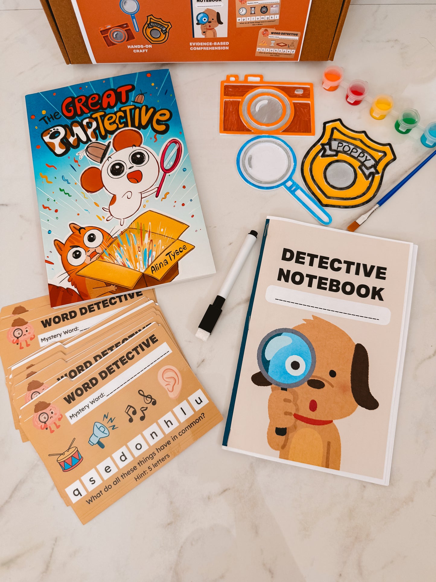 Detective-themed children's activity set with notebook, cards, and props on a marble surface.