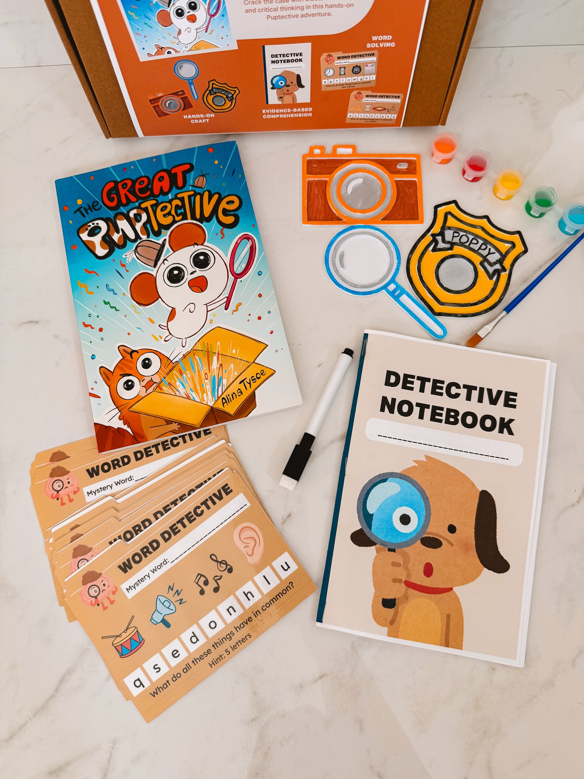 Children's detective-themed educational materials including a book, notebook, and cards on a light surface.