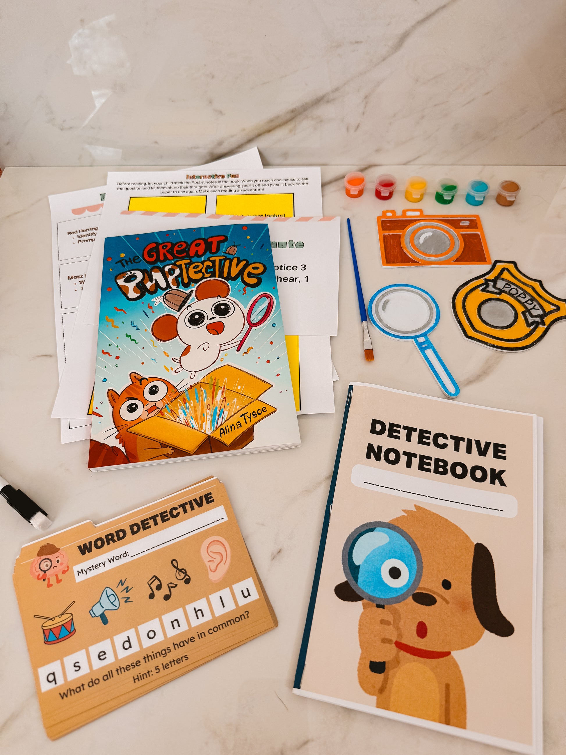 Children's detective-themed activity set with notebook, cards, and stationery on a marble surface.