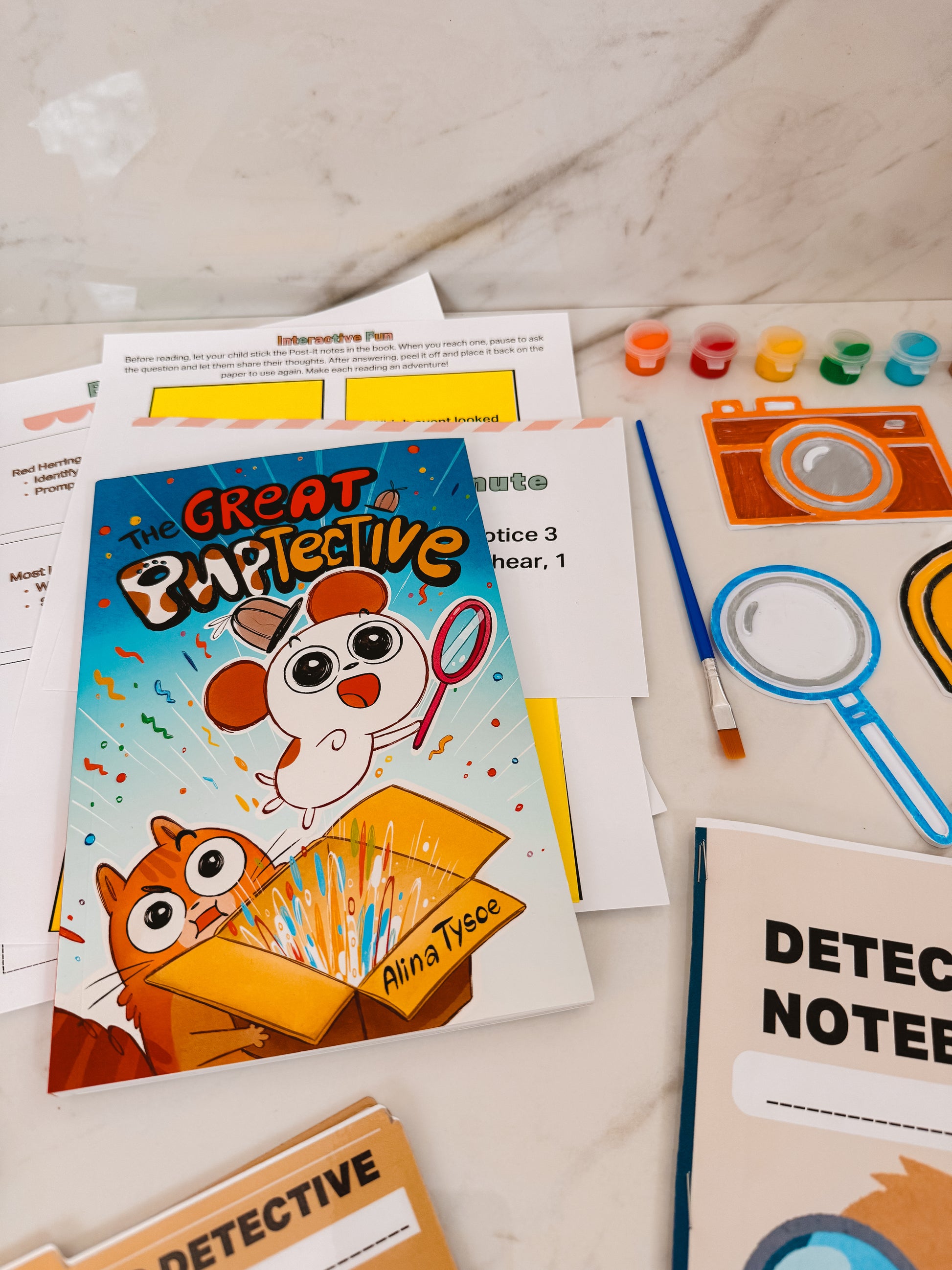 Children's educational materials including a book titled 'The Great Papercraftive' on a marble surface.