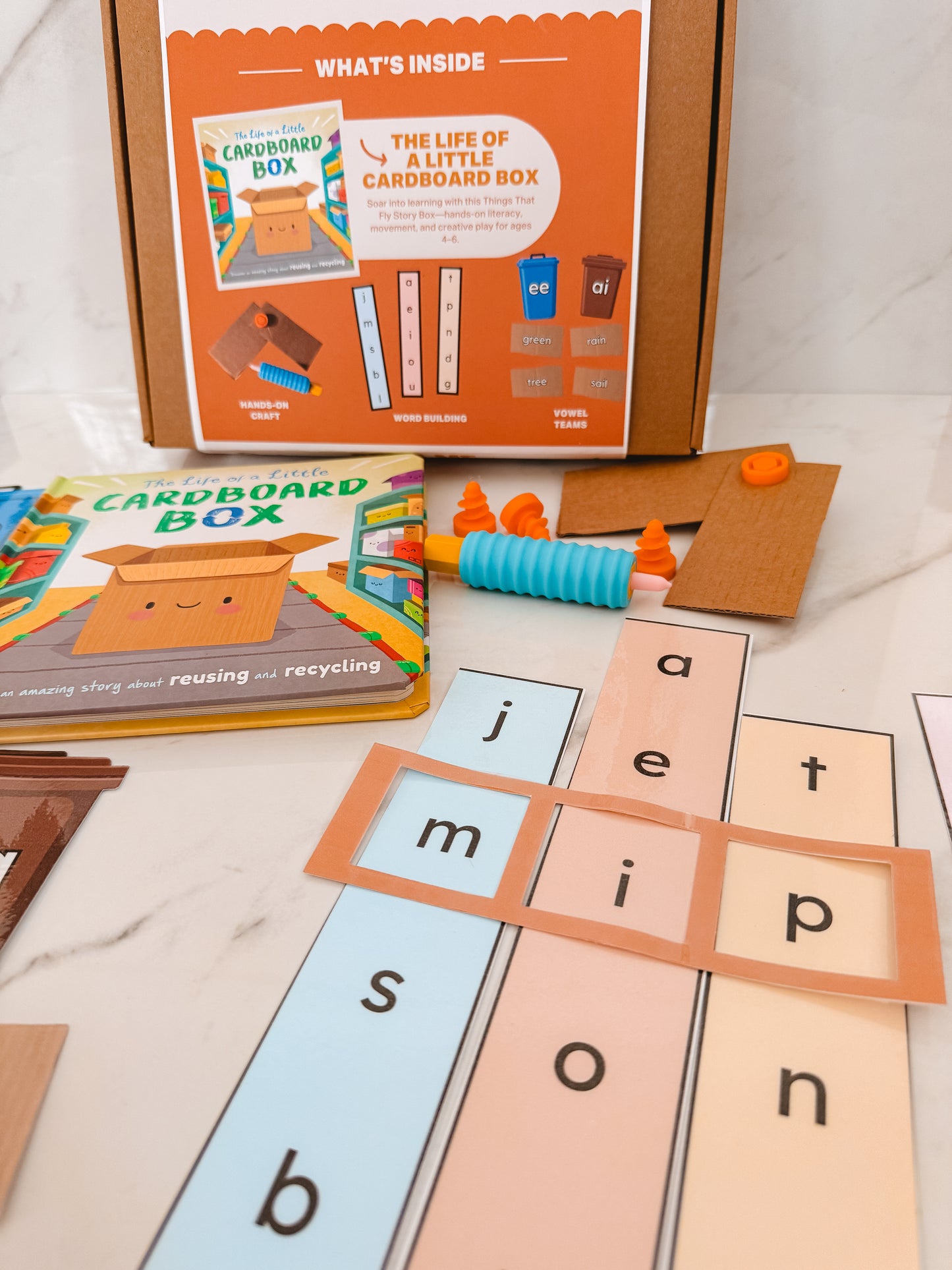 Educational materials including a cardboard box, alphabet cards, and a book on a marble surface.