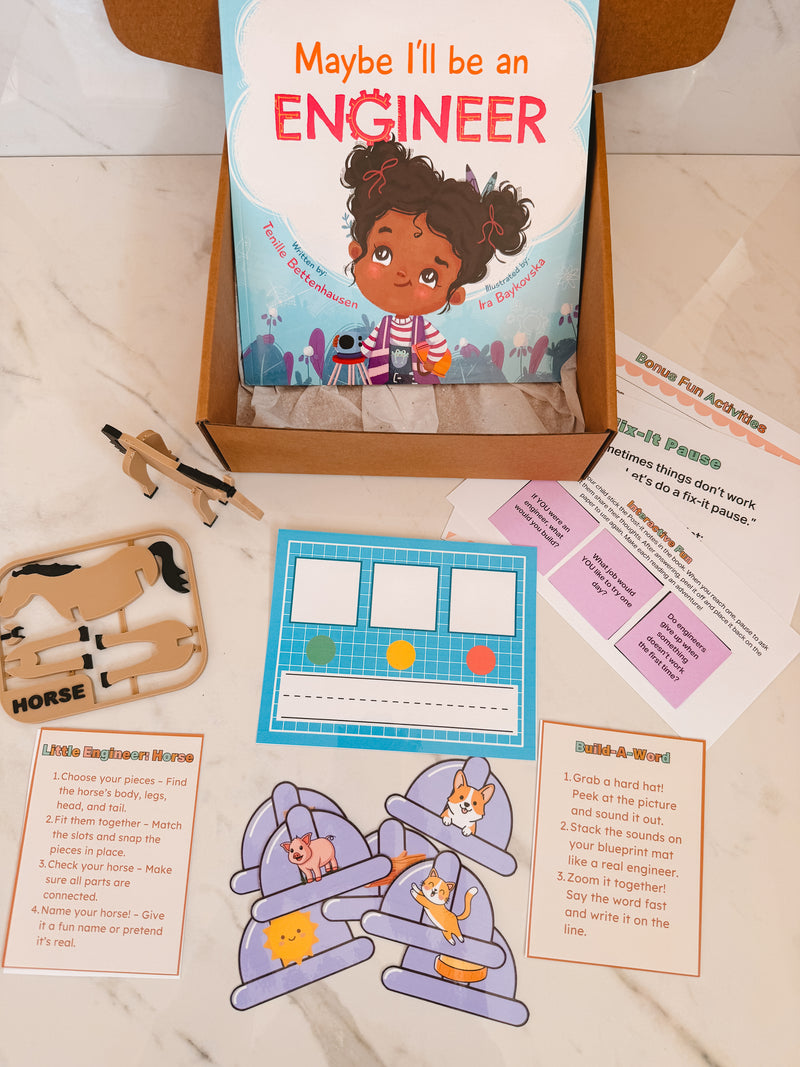 Educational materials including a book titled 'Maybe I'll be an Engineer', wooden horse, and paper cutouts on a marble surface.