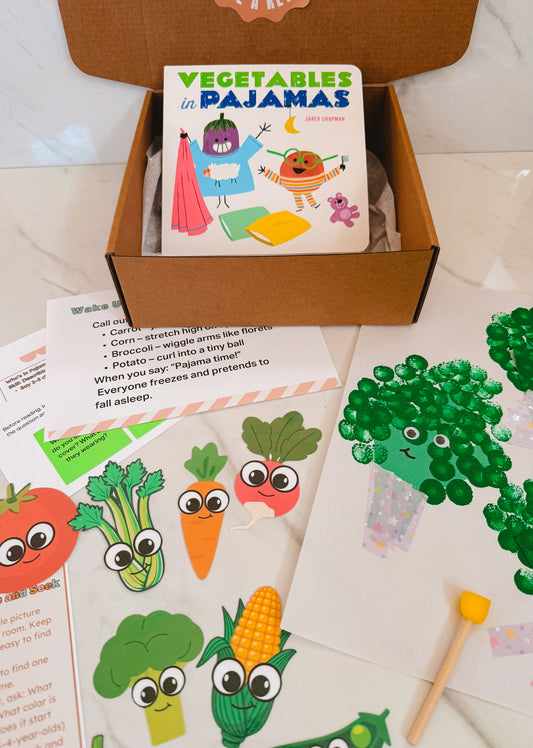 Children's book titled 'Vegetables in Pajamas' in a box with educational materials on a light surface.