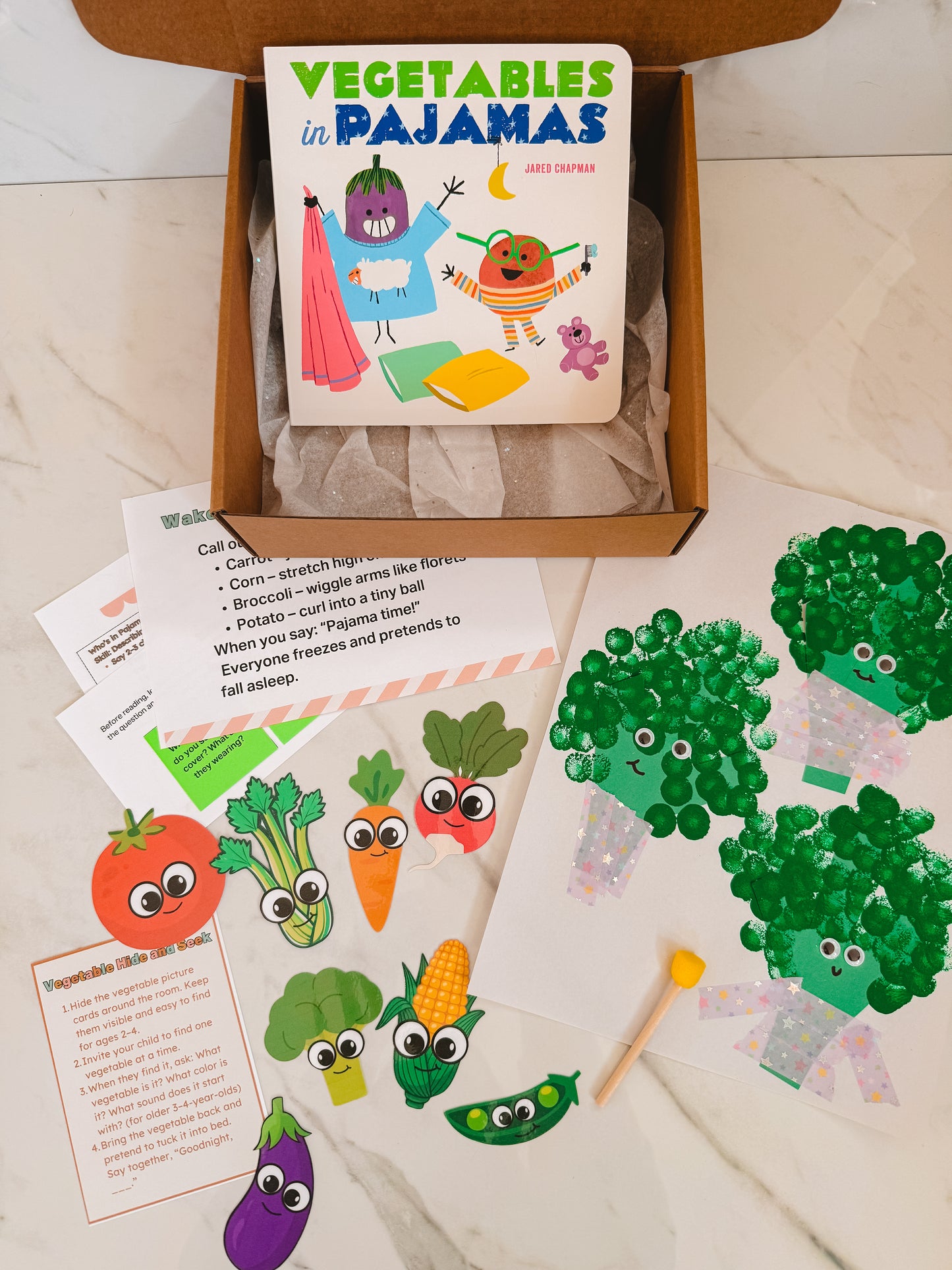 Children's book titled 'Vegetables in Pajamas' with matching finger puppet set on a wooden surface.