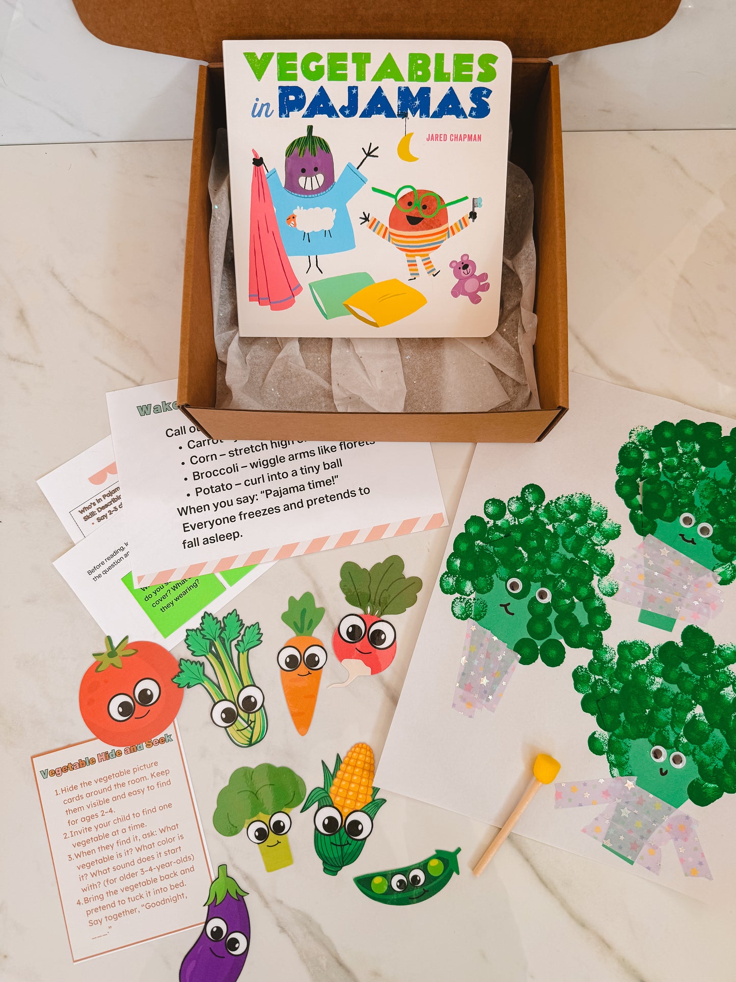 Children's book titled 'Vegetables in Pajamas' with related craft materials on a wooden surface.
