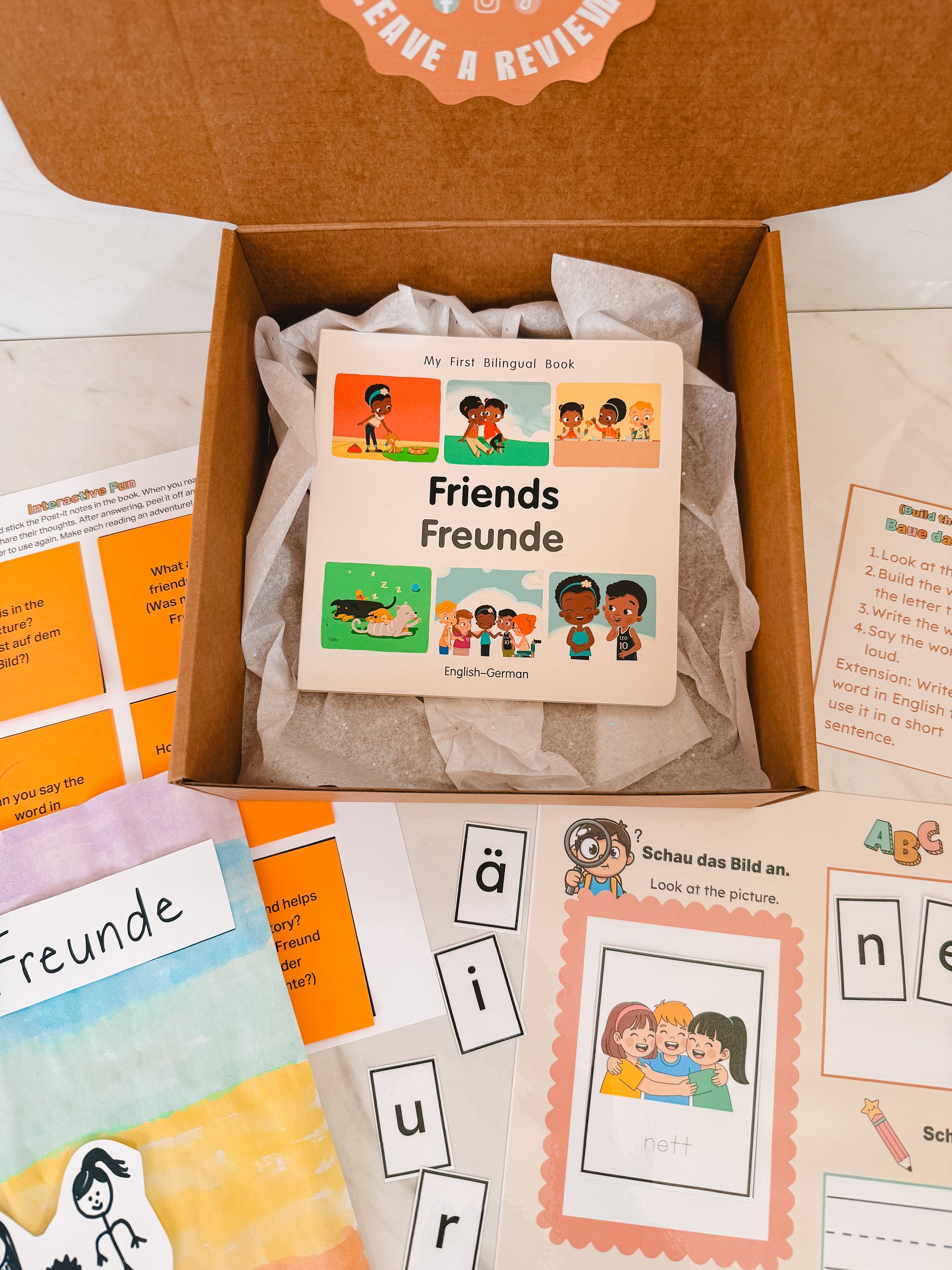 Educational materials including a book titled 'Friends Freunde' in English and German, flashcards, and activity sheets on a white background.