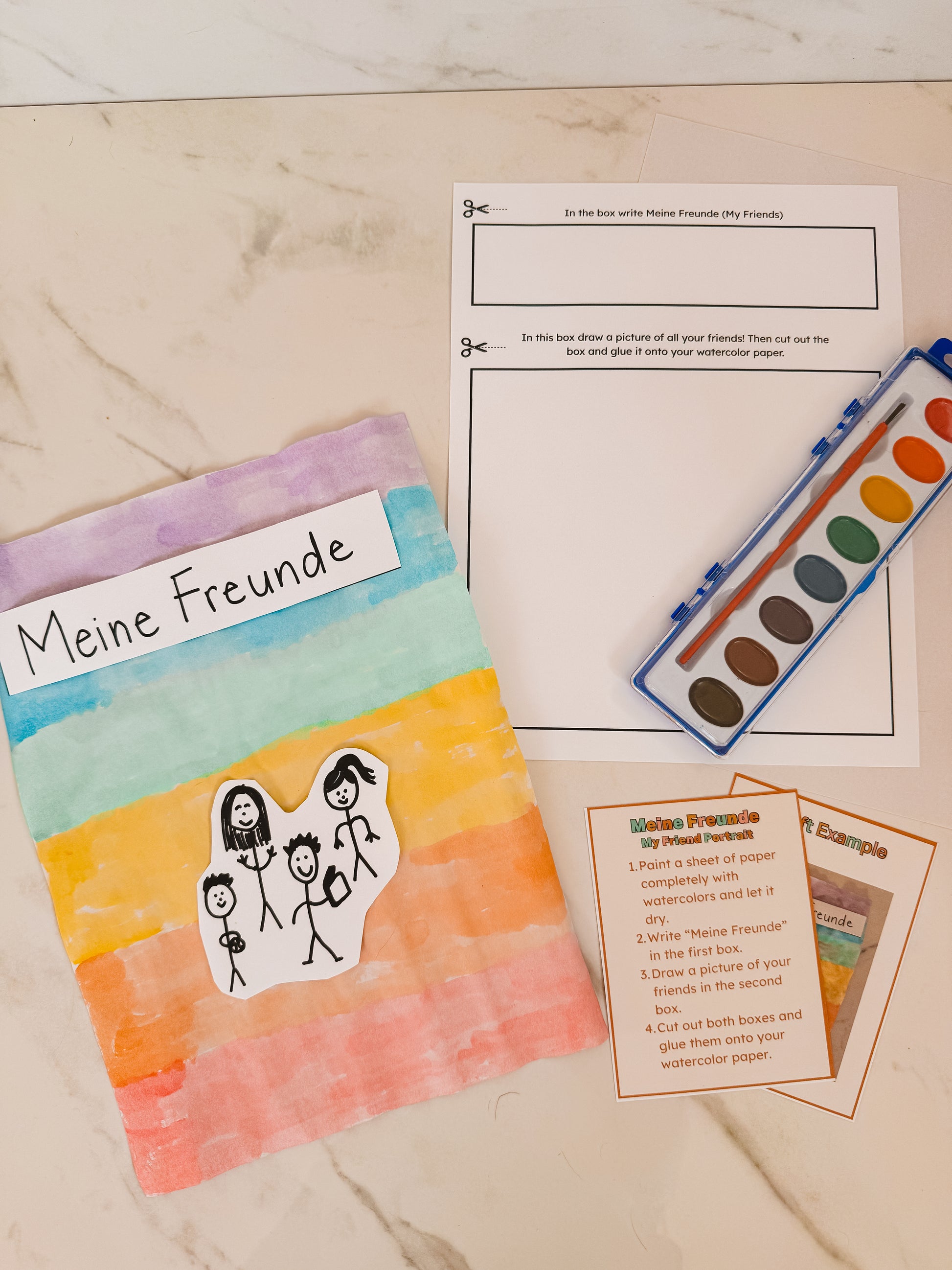 Colorful book titled 'Meine Freunde' with watercolor paint set and paper on a marble surface